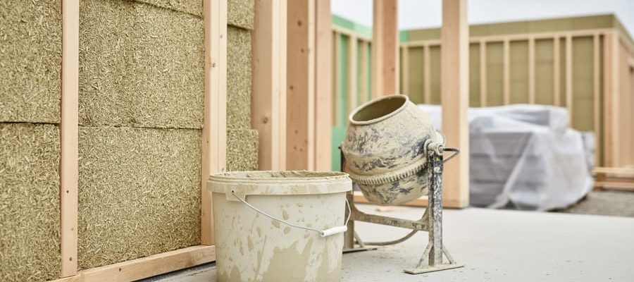 Hempcrete blocks in a timber-framed wall with a lime-based bucket and mortar mixer on a residential construction site.